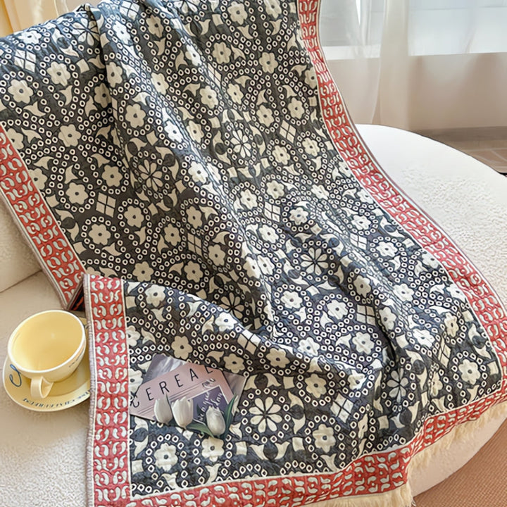 A patterned pure cotton bath towel draped over a white sofa with a yellow teacup and saucer nearby.