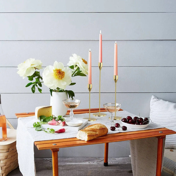 Three tall, slender stainless steel candle holders with pink taper candles on a wooden table.