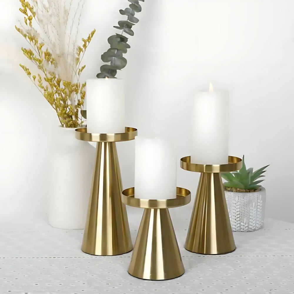Set of three artisan brass candle holders with white pillar candles on a white tablecloth.