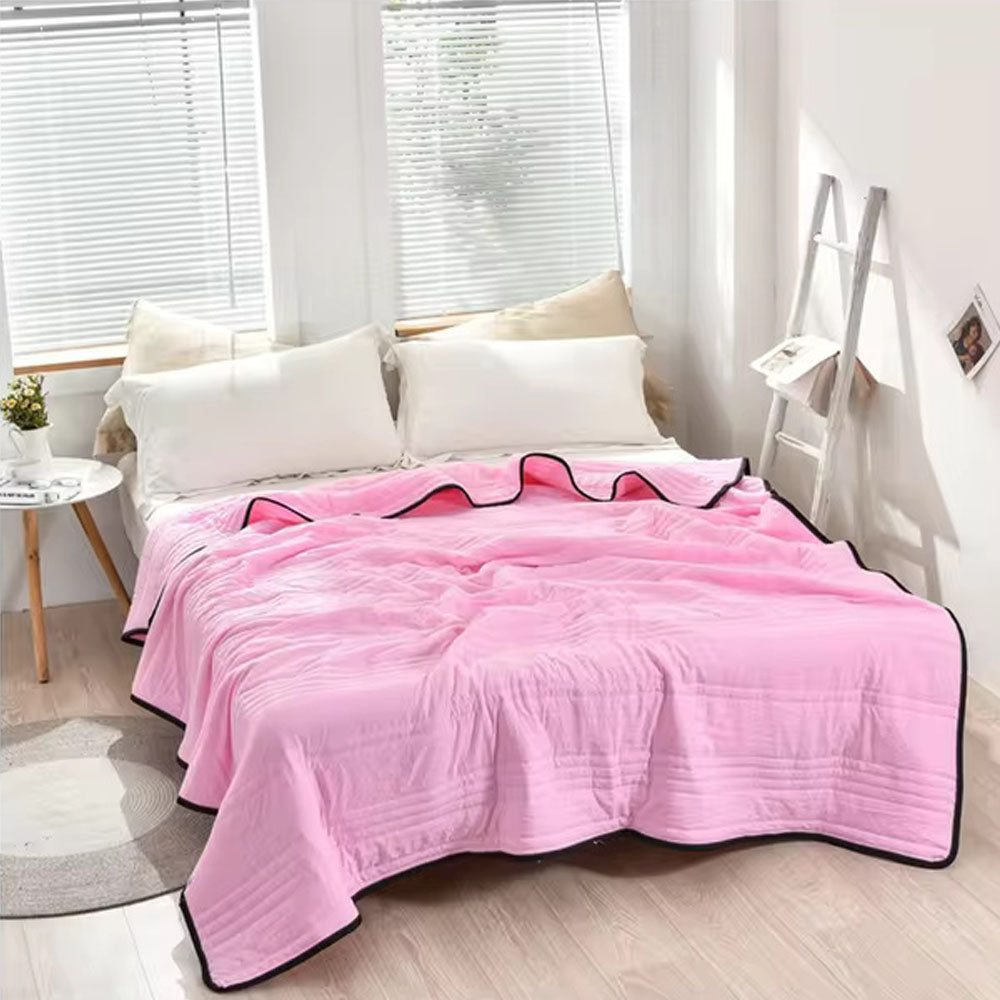 Pink EverChill Ice Cooling Blanket draped on a bed with white pillows.