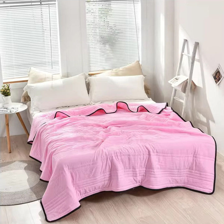 Pink EverChill Ice Cooling Blanket draped on a bed with white pillows.