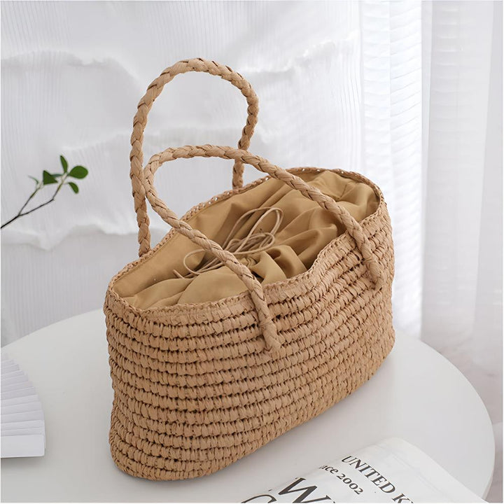 Handwoven straw tote bag with braided handles and a tan drawstring interior.