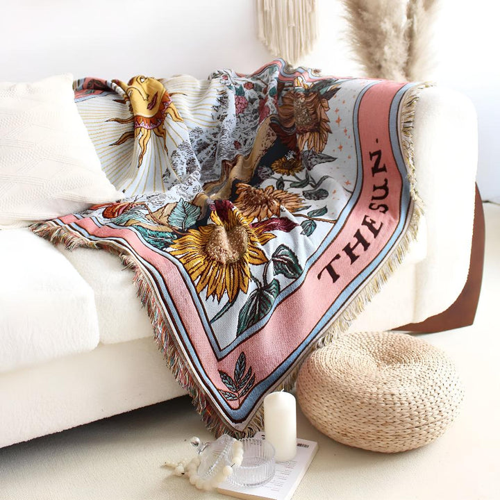 Boho style tapestry throw with a celestial sun tarot card design and fringe edges, draped on a white sofa.