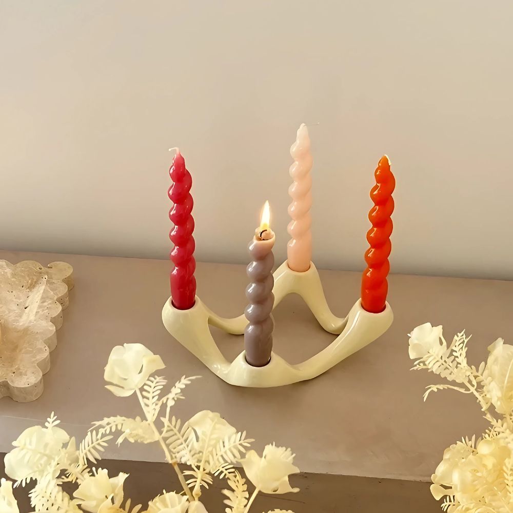 Ceramic candle holder with four twisted candles in red, gray, pink, and orange.