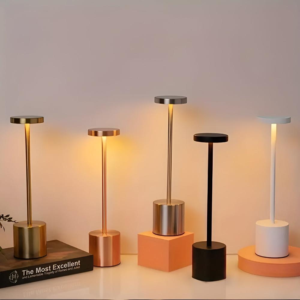 Five cordless table lamps in various colors: gold, rose gold, silver, black, and white, with warm light emanating from their tops.