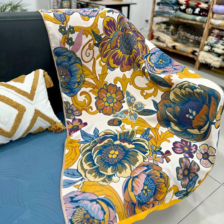 A reversible cotton bath towel with a vibrant blooming floral pattern in shades of blue, yellow, and orange on a white background.