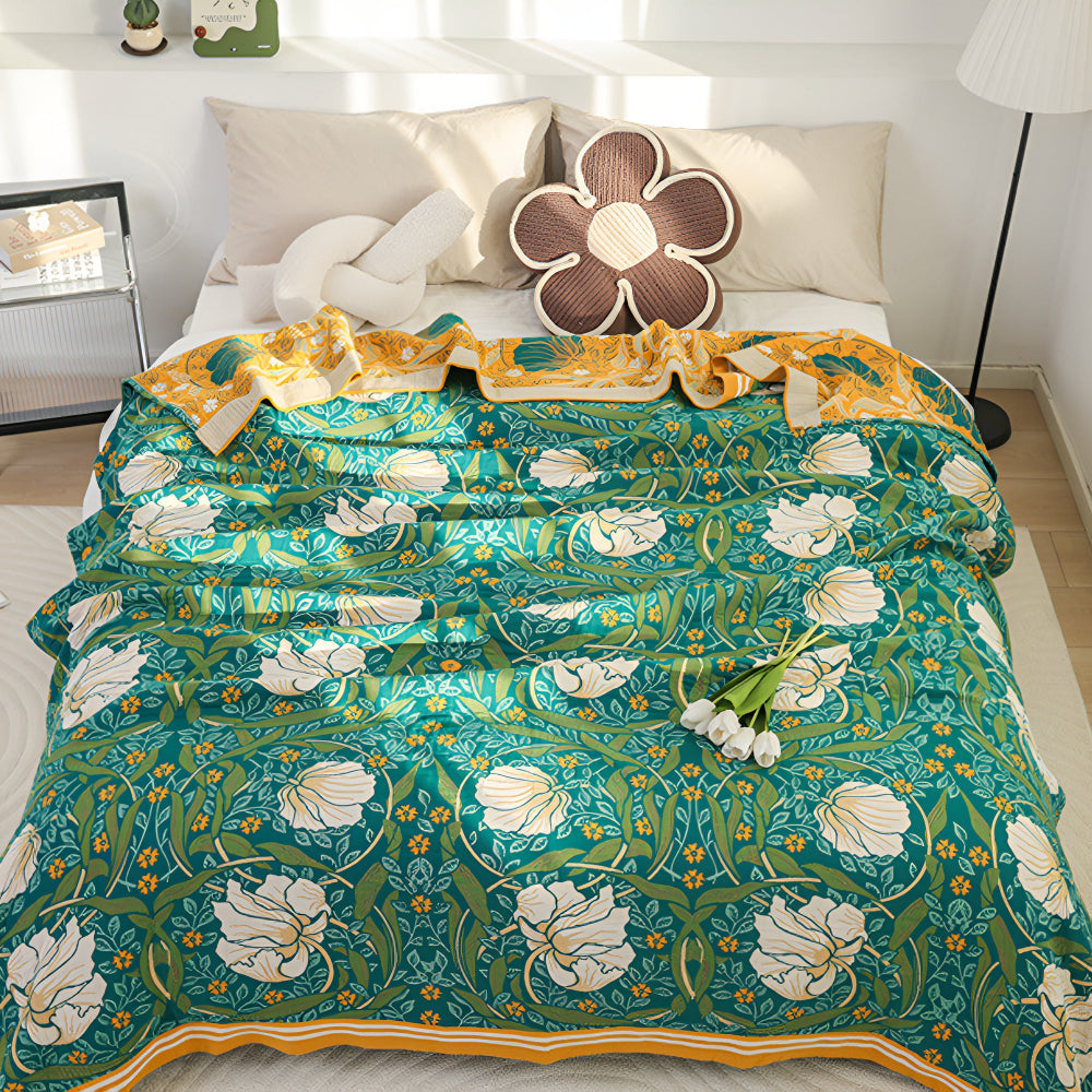 Green botanical bloom cotton blanket with white flowers and yellow accents, draped on a bed.