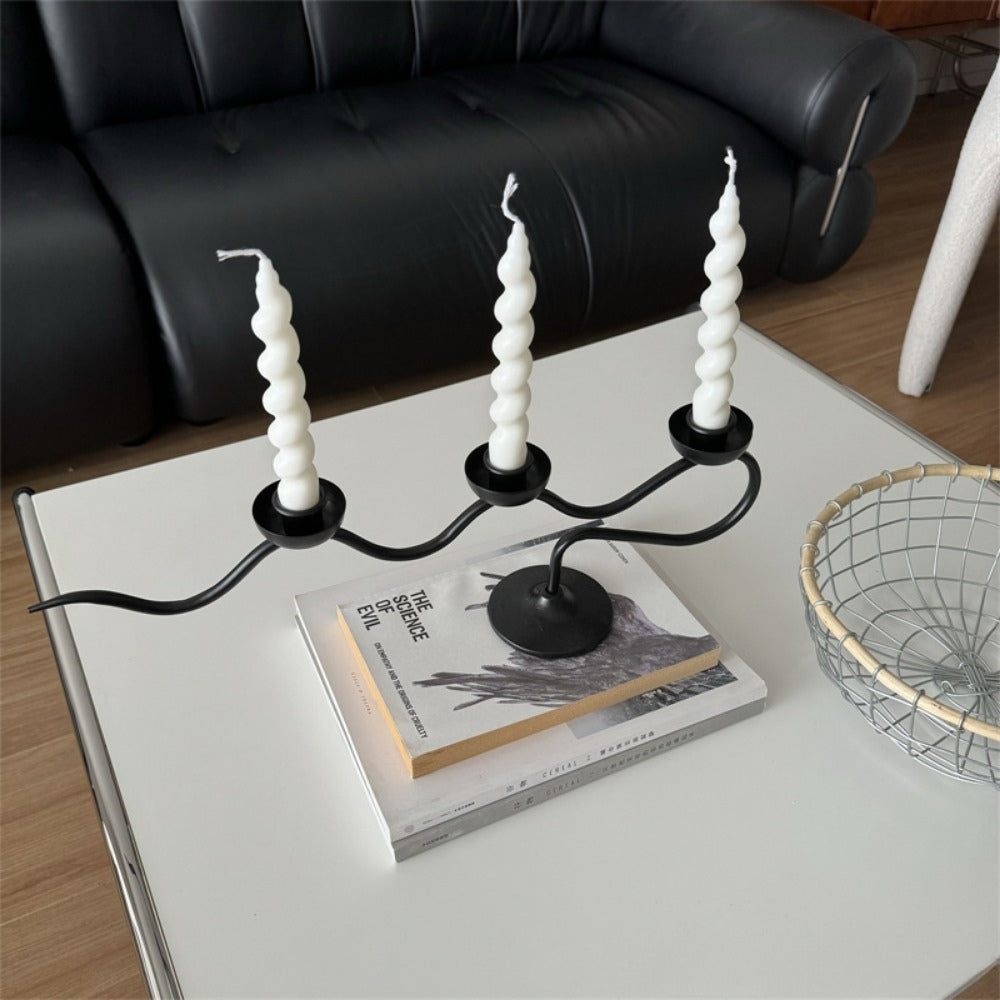 Black iron three-headed twisted candle holder with three white spiral candles on a white table.