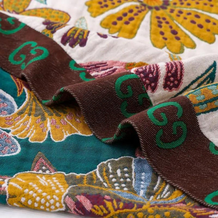 Brown trim with green GG logo on a floral patterned blanket in green, yellow, and white.