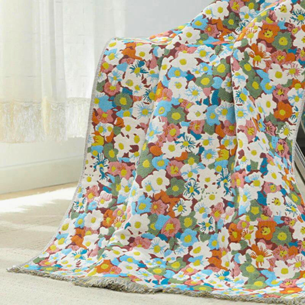 A soft, reversible cotton bath towel draped over a chair, featuring a vibrant floral pattern with white, pink, blue, and orange flowers.