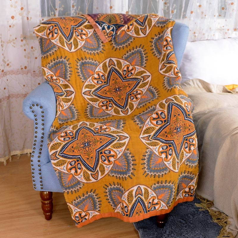A yellow throw blanket with a repeating orange, blue, and grey starburst pattern draped over a blue armchair.