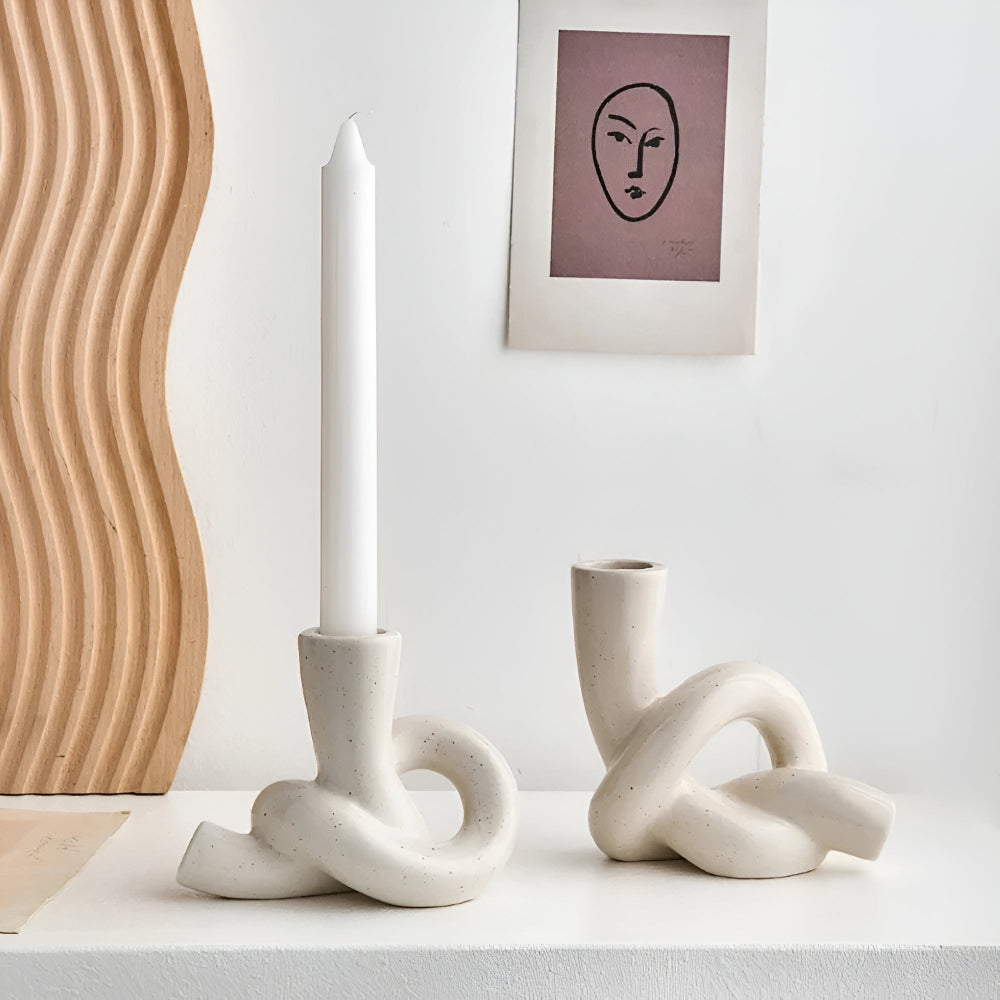 White ceramic candle holder with a knot design holding a white candle.
