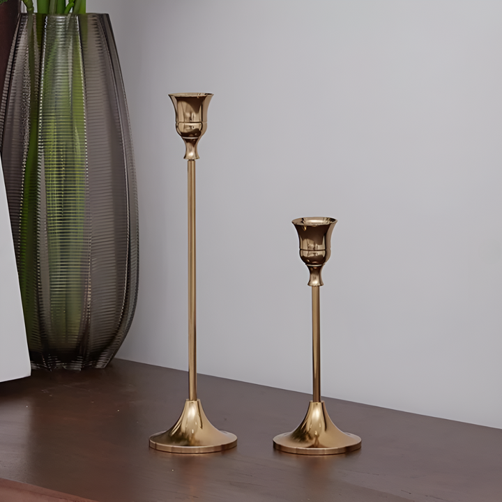 Two gold taper candle holders of different heights on a dark wooden surface.