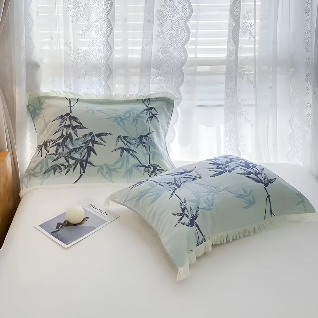 Two pillows with a light blue bamboo pattern and fringed edges on a white bed.