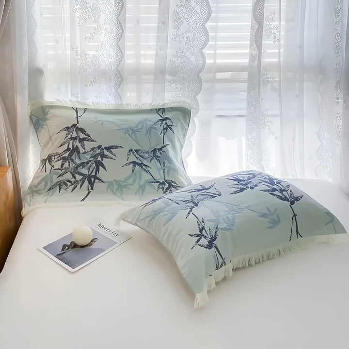 Two pillows with a light blue bamboo pattern and fringed edges on a white bed.