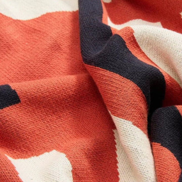 Close-up of a knitted blanket with a pattern of abstract orange, cream, and navy shapes.