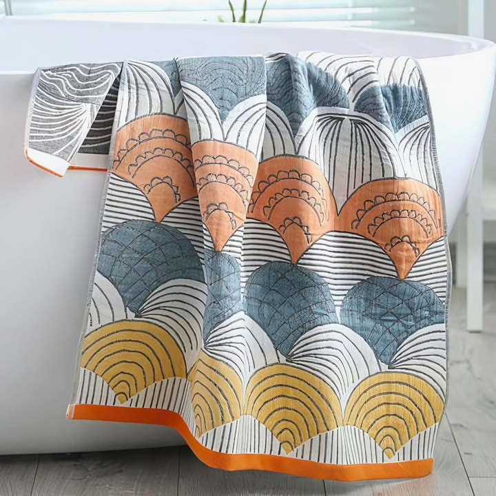 Cotton bath towel with a repeating abstract shell pattern in orange, blue, and yellow.