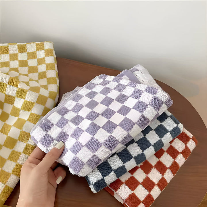 Stack of checkered cotton towels in purple, dark blue, and rust orange, with a yellow checkered towel in the background.