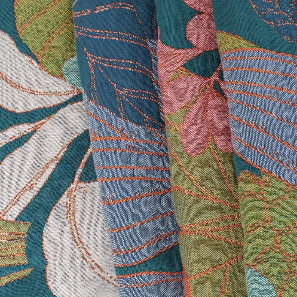 Close-up of a woven cotton gauze blanket with a garden-inspired floral and leaf pattern in teal, pink, green, and blue.