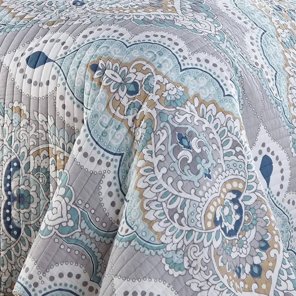 Close-up of a quilted coverlet with a paisley pattern in aqua, teal, and gray.