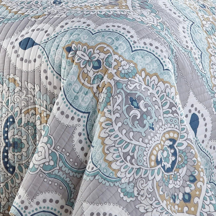 Close-up of a quilted coverlet with a paisley pattern in aqua, teal, and gray.