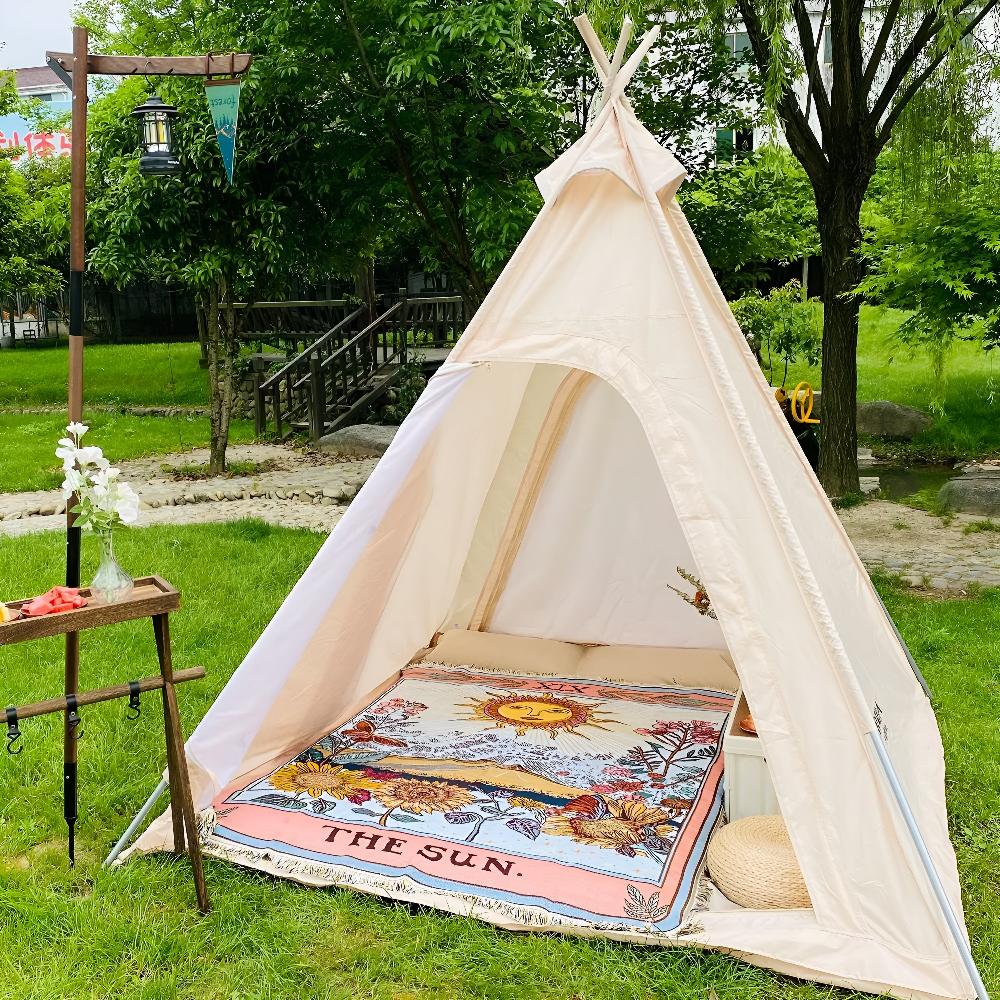 A celestial tapestry throw with a sun design is spread inside a teepee tent on a grassy lawn.