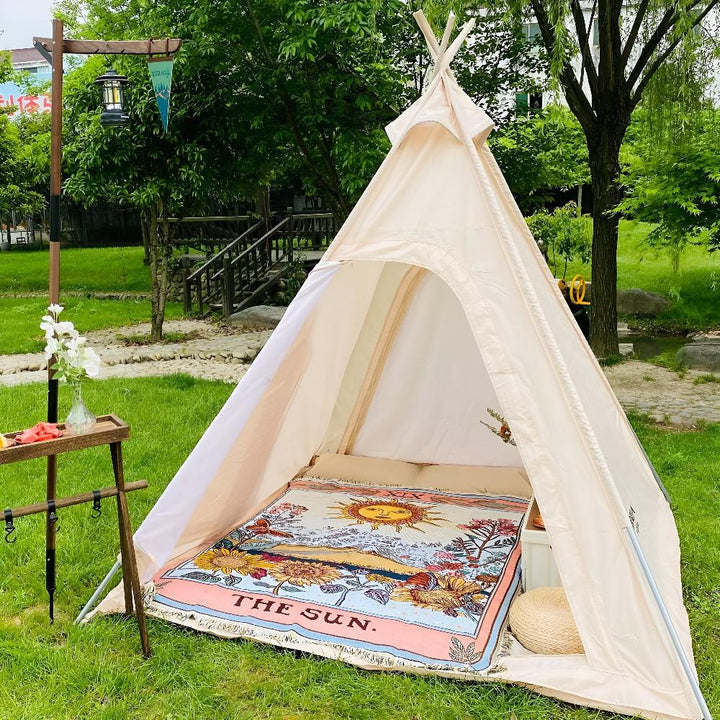 A celestial tapestry throw with a sun design is spread inside a teepee tent on a grassy lawn.