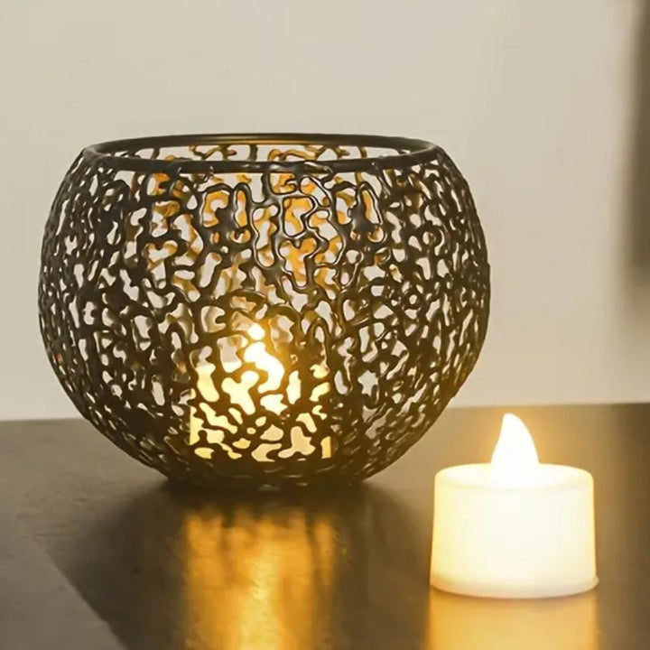 Black geometric iron tealight holder with a lit candle inside and a separate LED candle nearby.