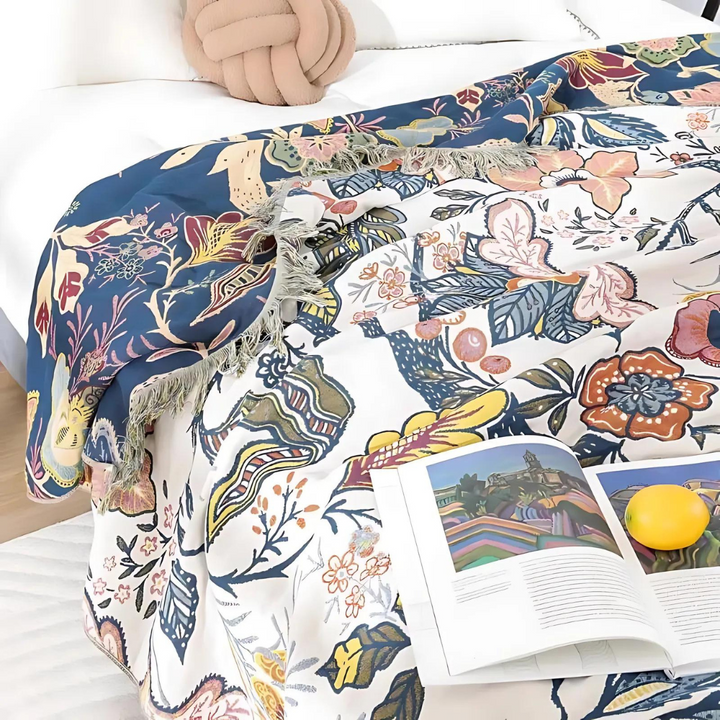 Rustic artistic flora cotton blanket with a blue and white floral pattern, draped on a bed with an open book and a lemon.
