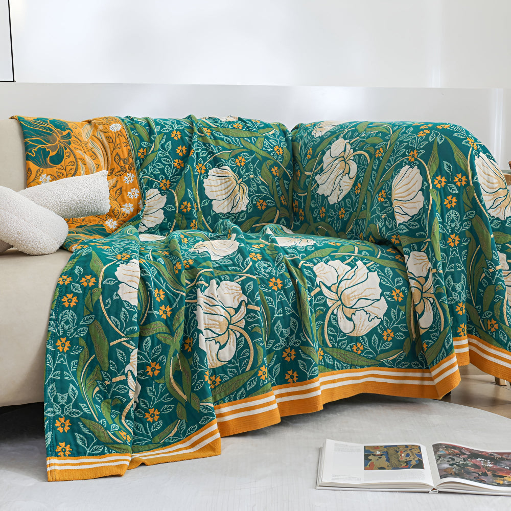Green botanical bloom cotton blanket draped over a sofa with two white pillows.