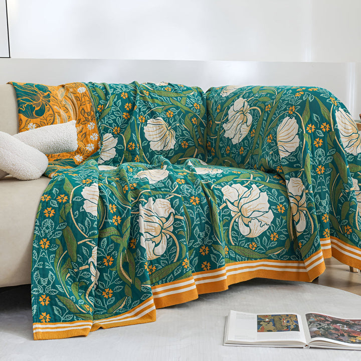 Green botanical bloom cotton blanket draped over a sofa with two white pillows.
