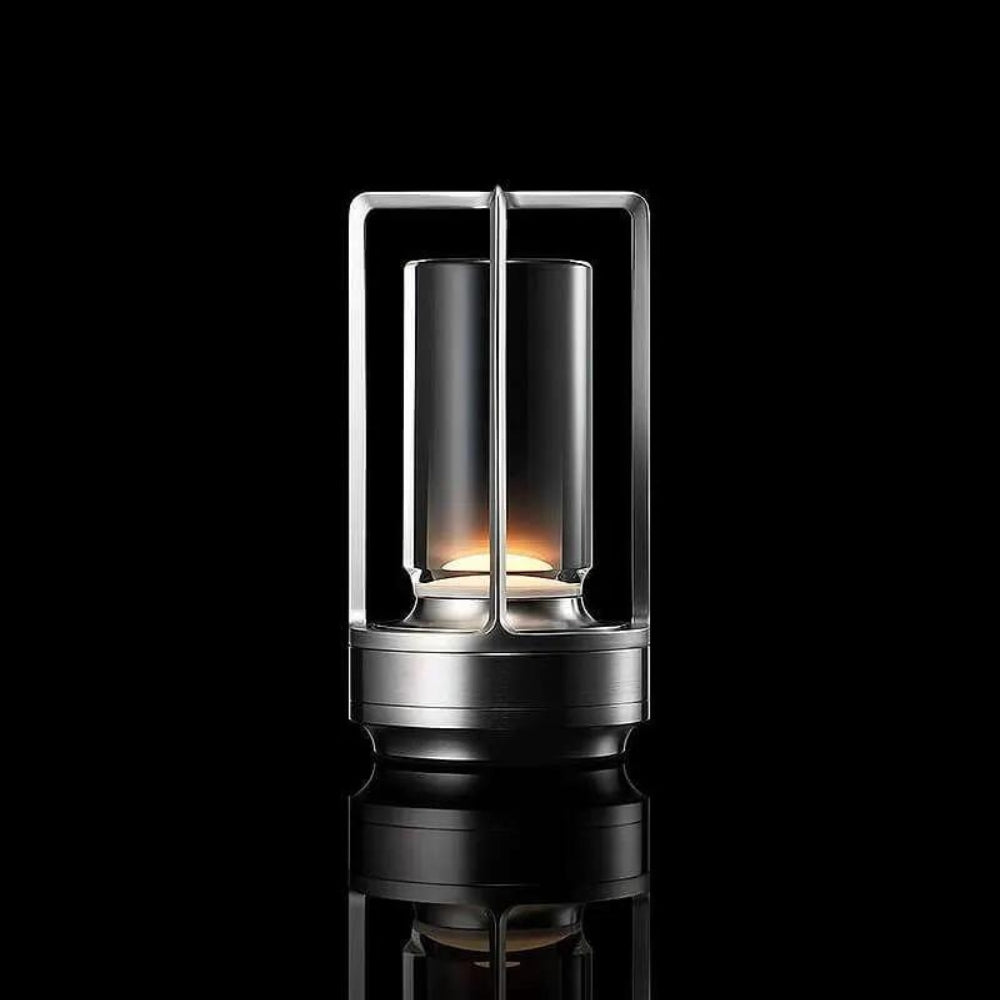 Crystal table lantern with a metallic base and a glass cylinder emitting warm light.