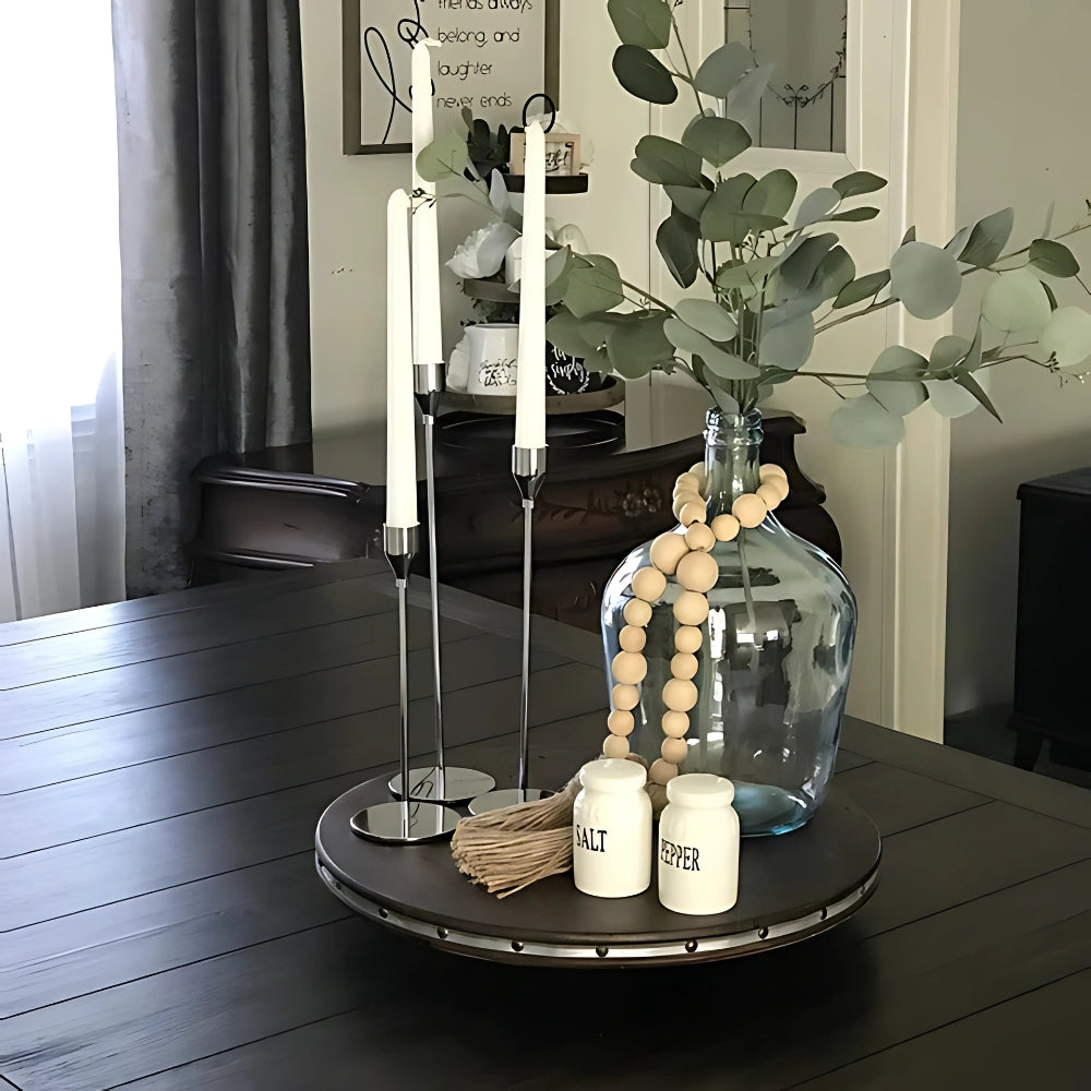 Three tall stainless steel candle holders on a wooden tray with candles.