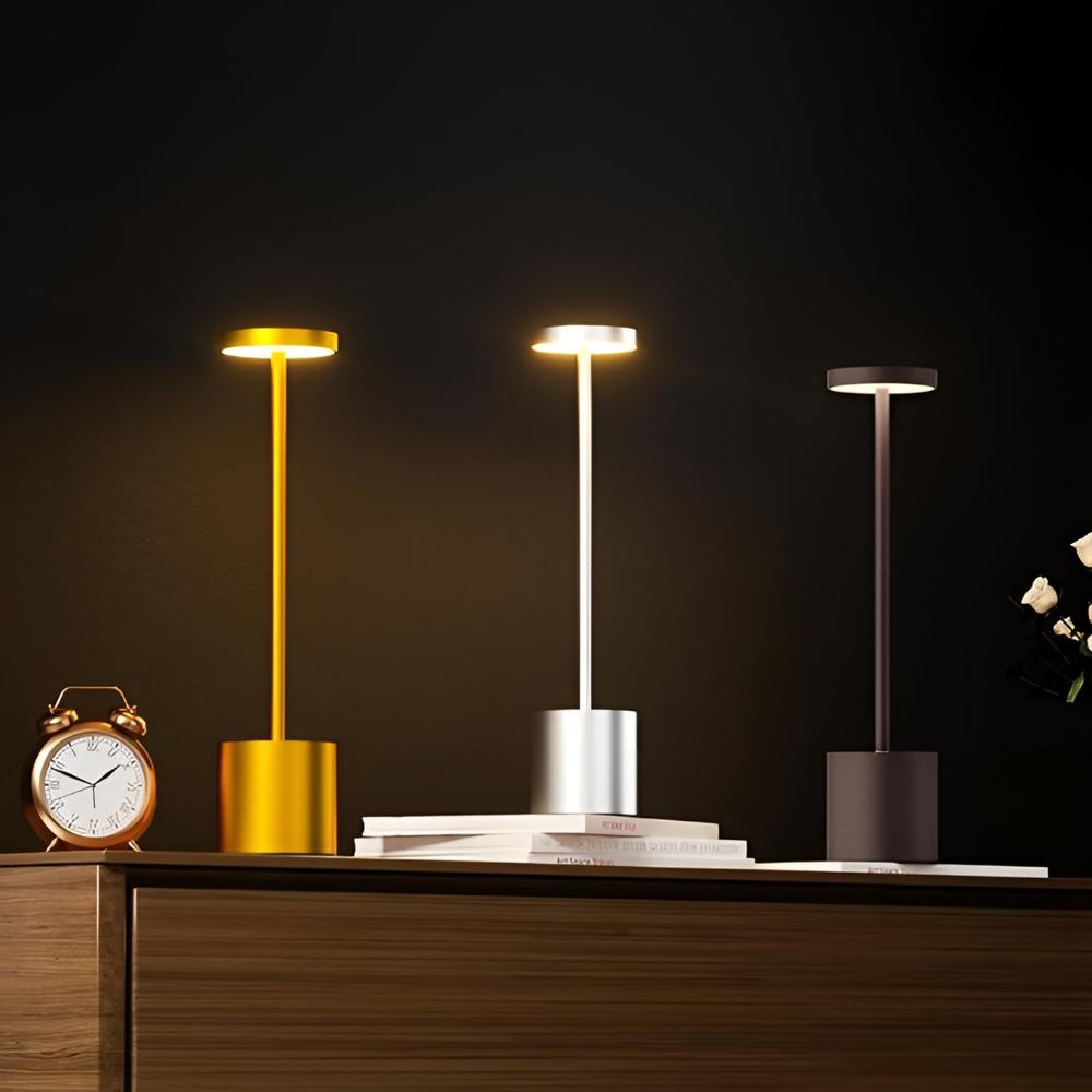 Three cordless table lamps in gold, silver, and dark gray, with warm light emanating from the top.