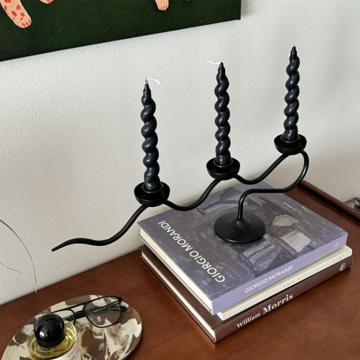 Black iron three-headed twisted candle holder with three black spiral candles.