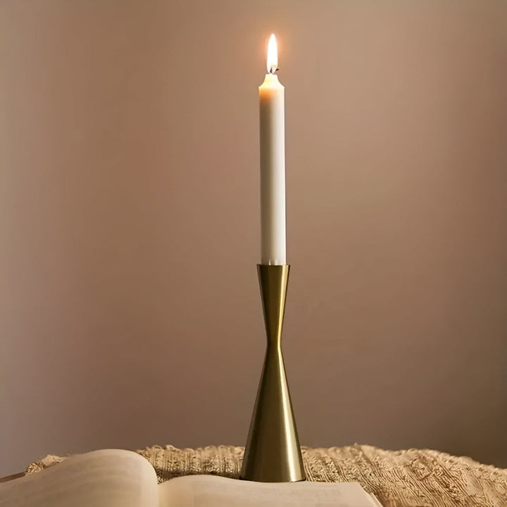 A single white taper candle in a brass waist-shaped candlestick on a textured cloth.