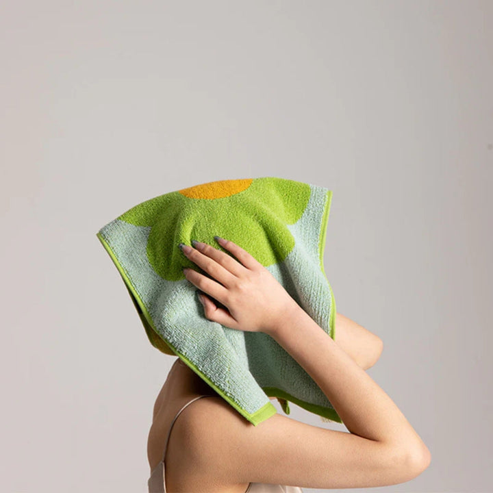 A person drying their face with a light green and yellow floral cotton bath towel.