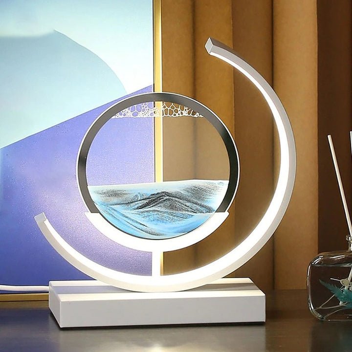 Modern desk lamp with a circular frame containing cascading sand and a curved LED light.