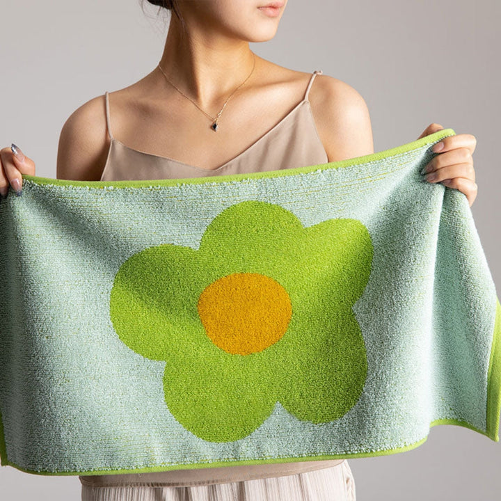A woman holds a light blue cotton bath towel with a large green and yellow flower design.