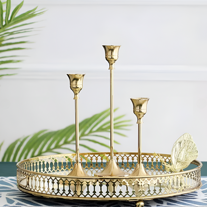 Set of three gold taper candle holders of varying heights on a decorative gold tray.