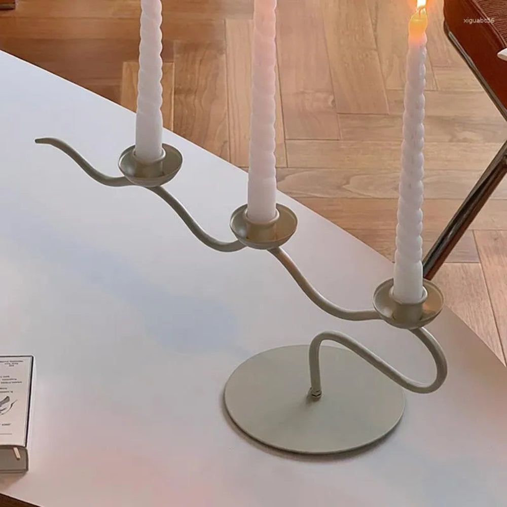A modern, three-headed twisted iron candle holder with white candles on a white surface.