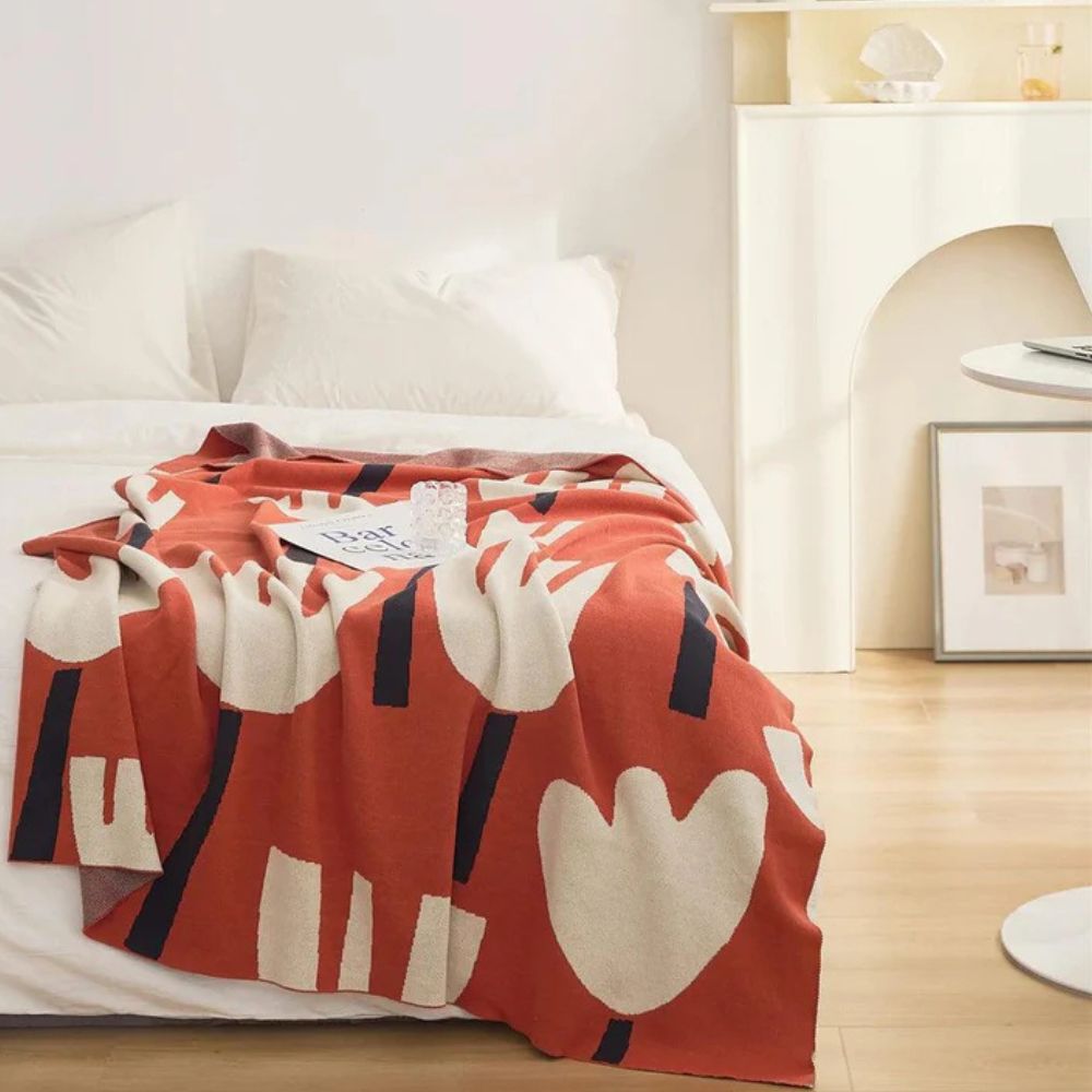 Orange knitted blanket with a cream and navy tulip floral pattern draped on a bed.