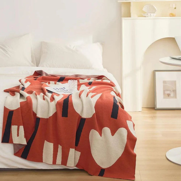 Orange knitted blanket with a cream and navy tulip floral pattern draped on a bed.