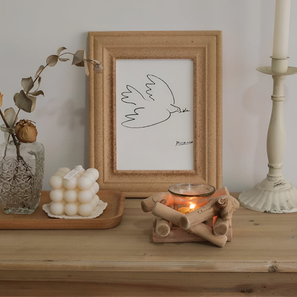 A lit tealight candle in a rustic driftwood holder on a wooden shelf.