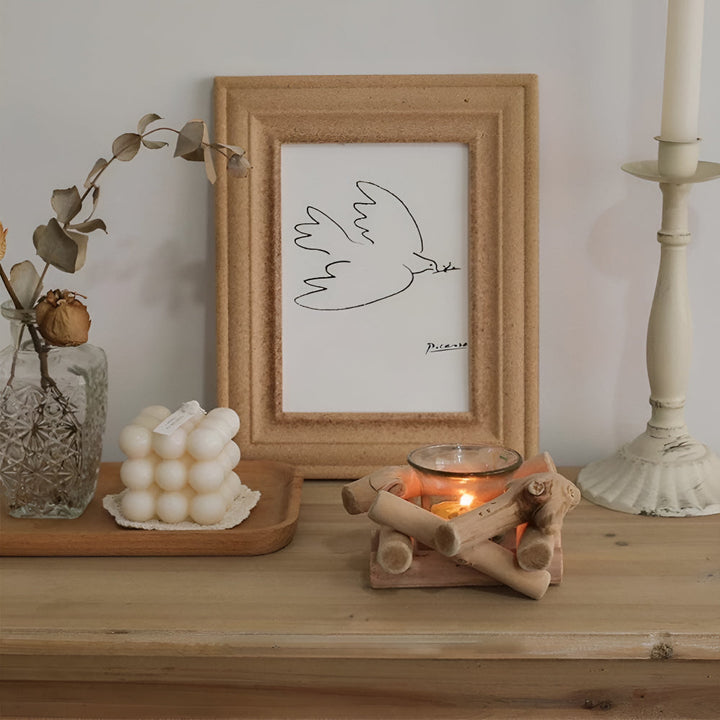 A lit tealight candle in a rustic driftwood holder on a wooden shelf.