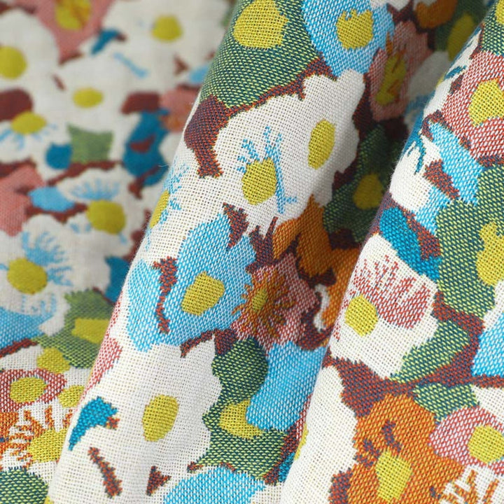 A close-up of a colorful floral patterned cotton fabric, featuring blue, yellow, green, and orange flowers on a white background.