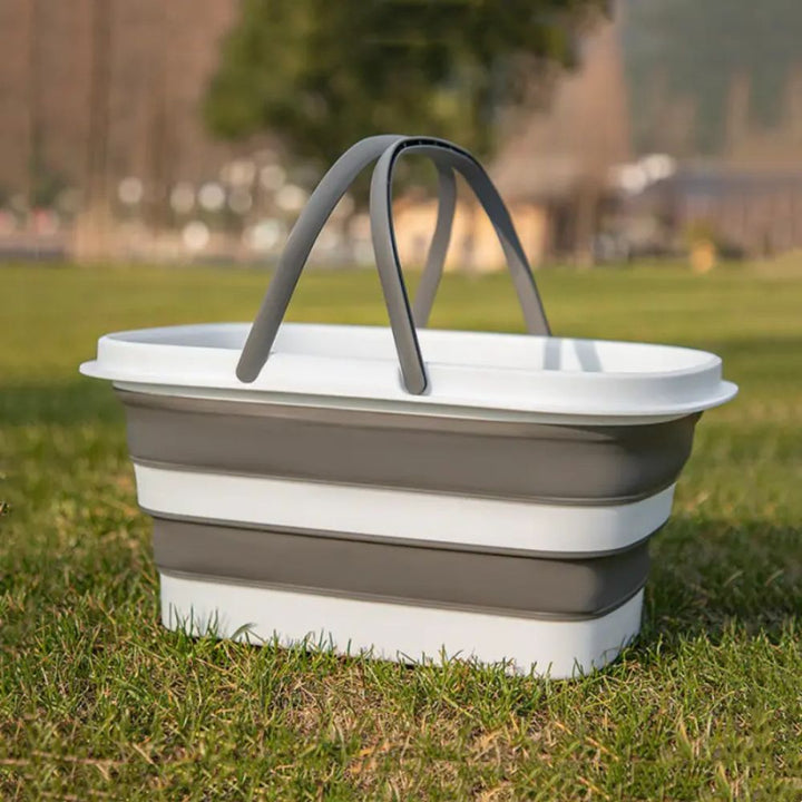 Collapsible storage basket with gray handles, made of white and gray plastic, sitting on green grass.
