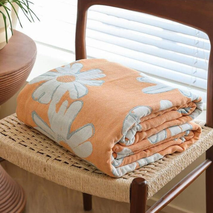 Orange cotton blanket with a large white daisy pattern, folded on a woven chair.