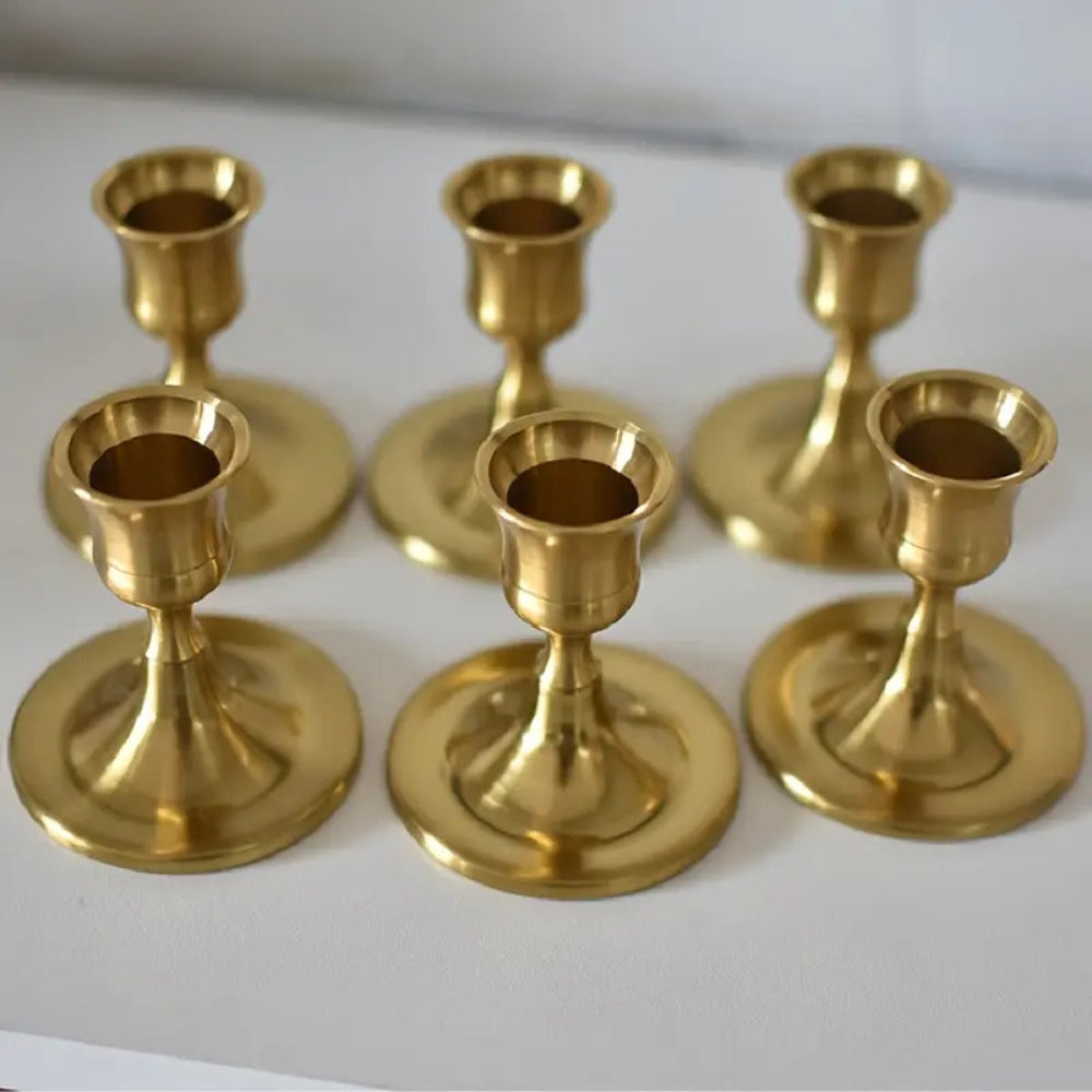 Six gold taper candle holders arranged in two rows on a white surface.