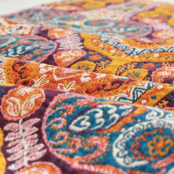 Close-up of a colorful boho-patterned cotton bath towel with paisley and floral designs in orange, teal, and yellow.